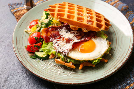 Delicious Belgian waffles with egg, bacon and vegetables in plate on table, closeup