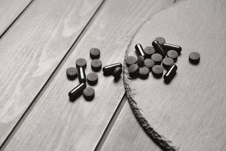 Board with activated carbon pills on dark wooden background