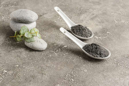 Spoons of activated carbon powder for facial mask and spa stones on grunge background