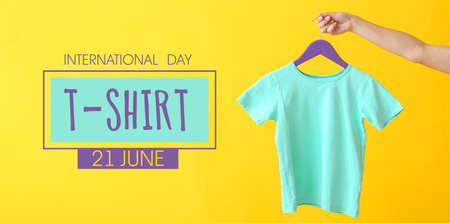 Woman holding hanger with baby t-shirt on color background. International T-Shirt Day