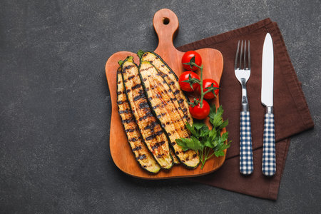Wooden board with tasty grilled zucchini and fresh tomatoes on dark backgroundの写真素材