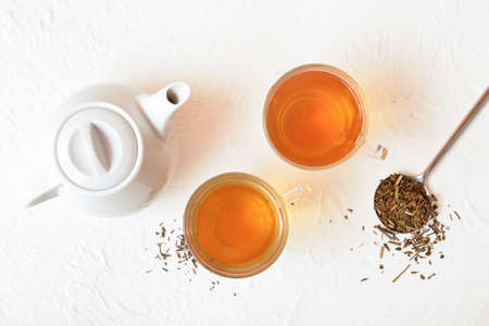 Glass cups of tasty hojicha tea, pot and dry leaves on white backgroundの写真素材
