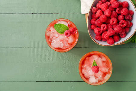 Glasses of tasty lemonade and bowl with raspberry on color wooden background
