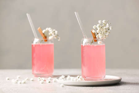 Glasses with tasty cocktail and beautiful gypsophila flowers on light background