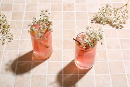 Glasses with tasty cocktail and beautiful gypsophila flowers on light tile background