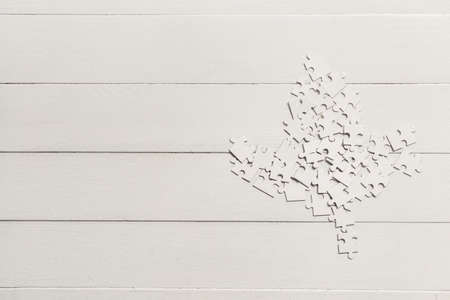 Maple leaf made of puzzle pieces on white wooden background. Canadian flag concept