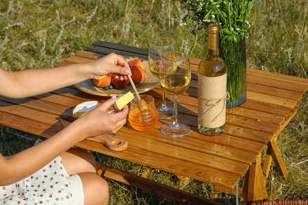 Young woman eating cheese with honey on romantic picnic outdoors