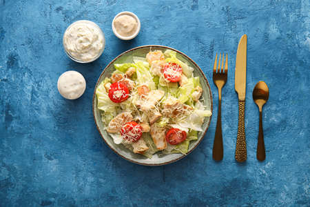 Plate of tasty Caesar salad and bowls with sauce on blue backgroundの写真素材