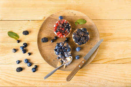 Plate with spoon and tasty berry tartlets on wooden background