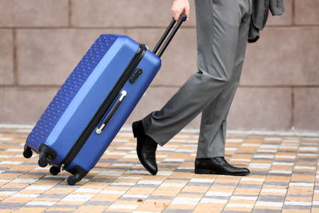Young businessman with blue suitcase walking outdoorsの写真素材