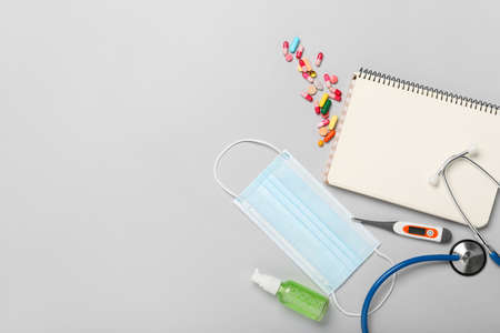Medical mask, notebook and medications on light background