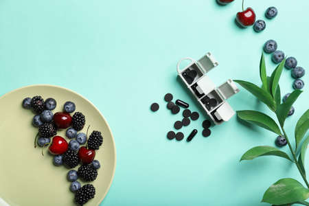 Activated carbon in capsules, pills and berries on color backgroundの写真素材
