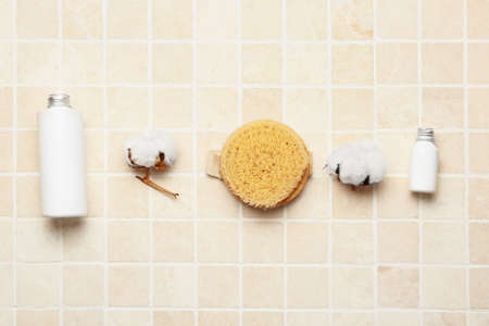 Bottles of cosmetic products, massage brush and cotton flowers on light tile