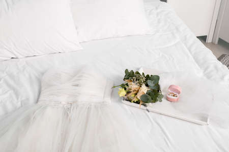 Beautiful wedding dress, rings and bouquet on bed