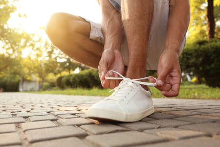 Sporty young man tying shoe laces outdoors