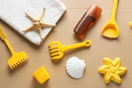 Set of beach accessories for children, towel and bottle of sunscreen on color wooden background