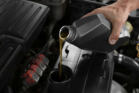 Male mechanic pouring motor oil from canister into car engineの写真素材