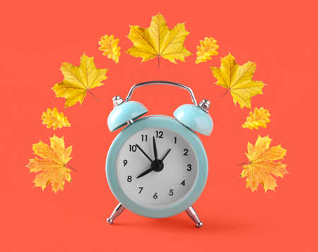 Alarm clock with autumn leaves on orange background. daylight saving timeの写真素材