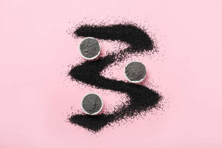 Composition with bowls of activated carbon facial mask and powder on color background