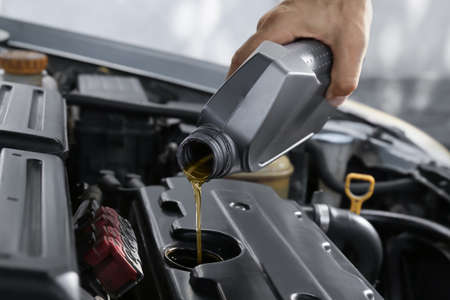 Male mechanic pouring motor oil from canister into car engineの写真素材