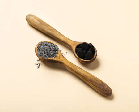 Wooden spoons with activated carbon facial mask and pills on color backgroundの写真素材