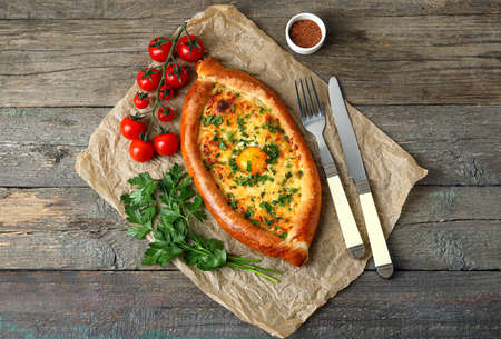 Parchment with tasty Ajarian khachapuri and tomatoes on wooden backgroundの写真素材