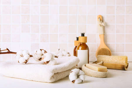 Set of bath supplies and cotton branch on table against tile wallの写真素材