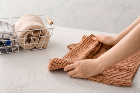 Woman folding clothes on light background, closeup