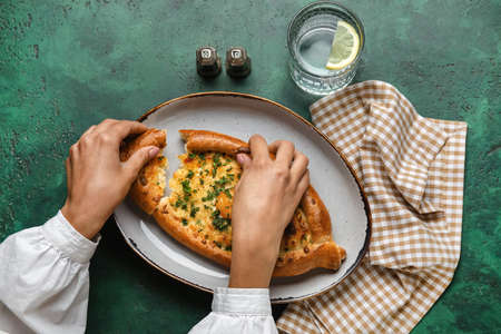 Woman eating tasty Ajarian khachapuri on color background