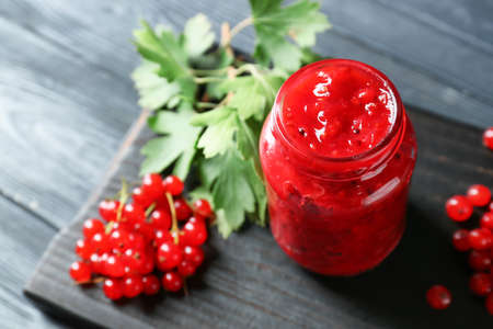 Jar of tasty red currant jam and berries on dark wooden background, closeup