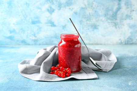 Jar of tasty red currant jam and berries on color background