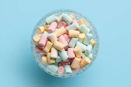 Glass bowl with marshmallows on blue background