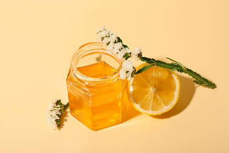 Jar of sweet honey, lemon and flowers on color background