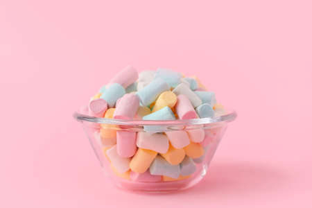 Glass bowl with sweet marshmallows on pink background