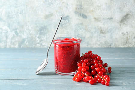 Jar of tasty red currant jam and spoon on table