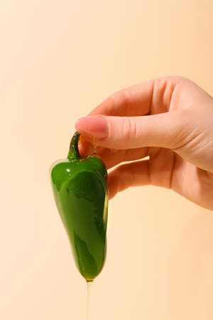 Woman holding jalapeno pepper with honey on color background, closeup