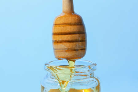 Pouring of sweet honey from dipper on color background, closeup