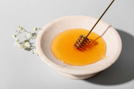Bowl of sweet honey, dipper and flowers on gray backgroundの写真素材