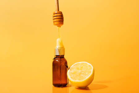 Pouring of honey from dipper onto bottle of essential oil on color background, closeup