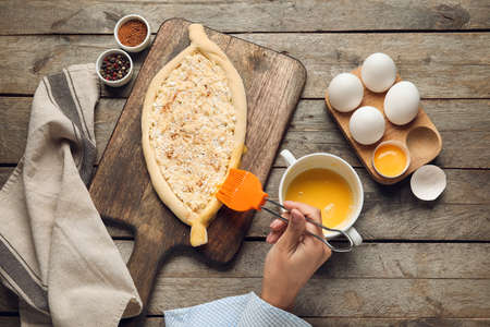 Woman preparing homemade Ajarian khachapuri on wooden table backgroundの写真素材