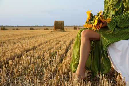 Romantic young woman with sunflowers on harvested field backgroundの写真素材