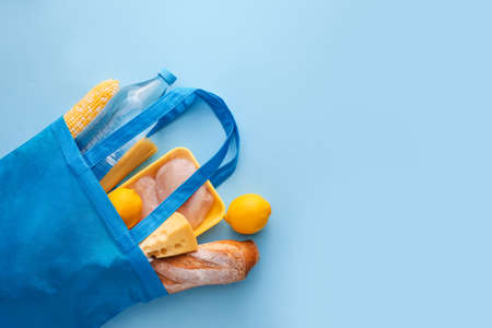 Eco bag with products, packed meat and bottle of water on color backgroundの写真素材
