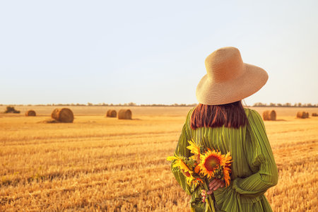 Romantic young woman with sunflowers on harvested field backgroundの写真素材