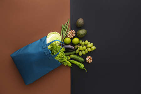 Eco bag with different scattered fruits and vegetables on black and brown backgroundの写真素材
