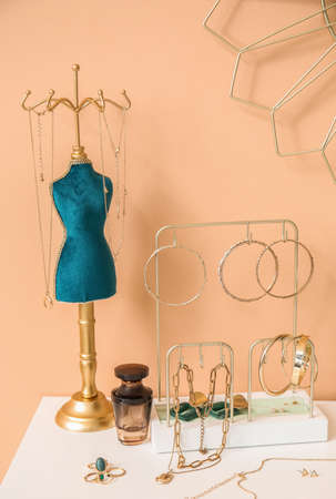 Stands with stylish jewelry and perfume bottle on white table near color wallの写真素材