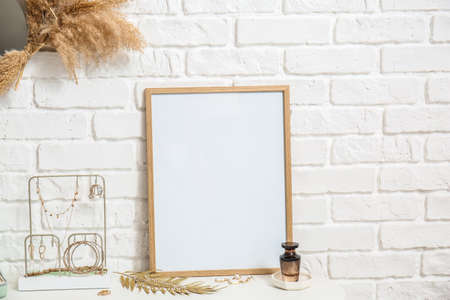 Stand with stylish jewelry, perfume bottle and blank photo frame on table near white brick wall