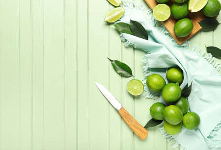 Tasty limes and knife on color wooden background
