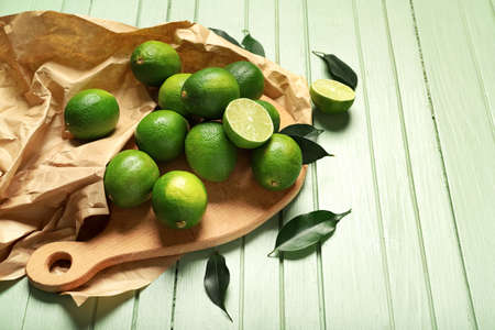 Board with tasty limes on color wooden background