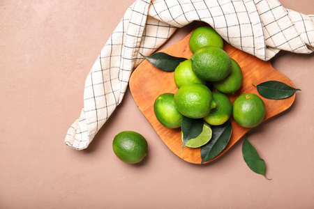 Board with tasty limes on color background
