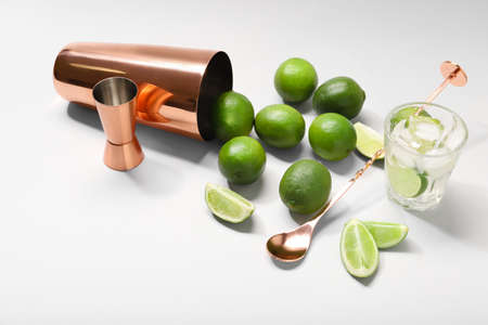 Glass of tasty cocktail, limes and shaker on white background